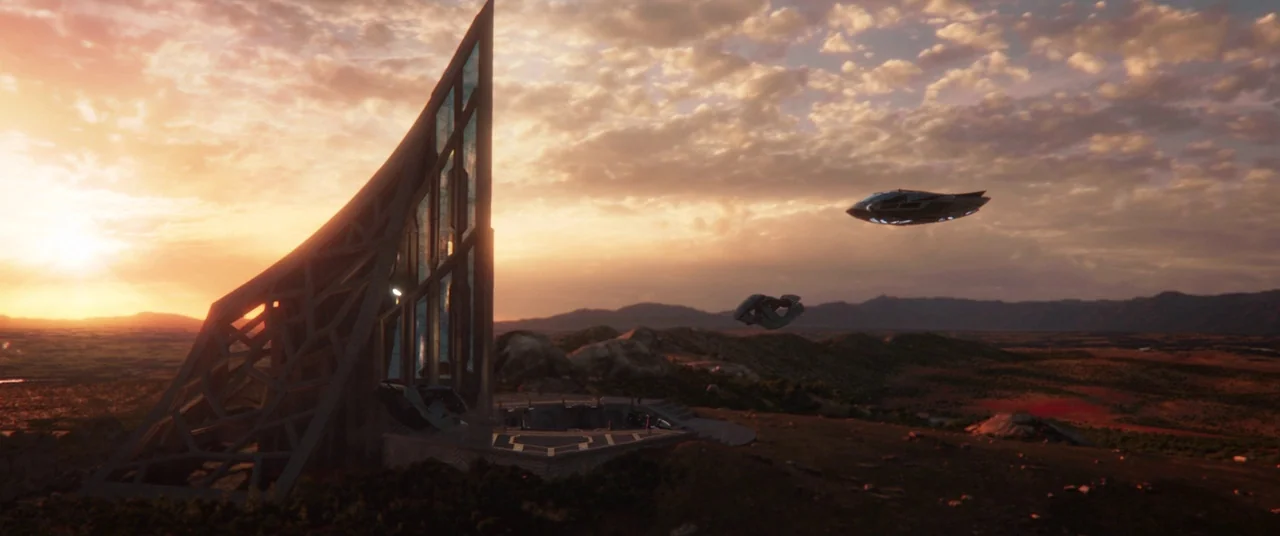 Black Panther (2018) movie still: establishing — A futuristic angular structure sits atop a rocky hill during a sunset. Small flying vehicles hover…