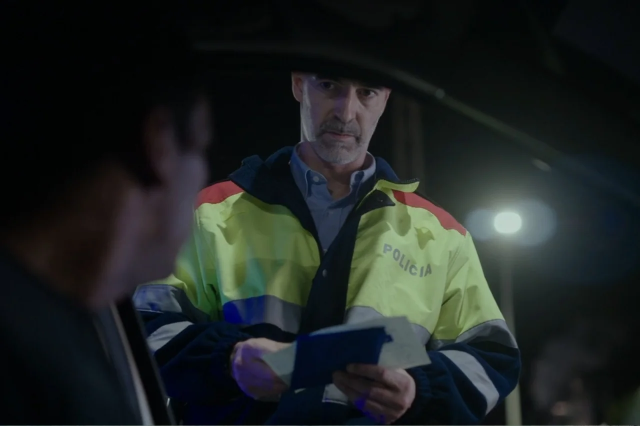 Cross the Line (2020) movie still: medium — A nighttime roadside stop shows a police officer standing beside a parked vehicle. The officer holds a…