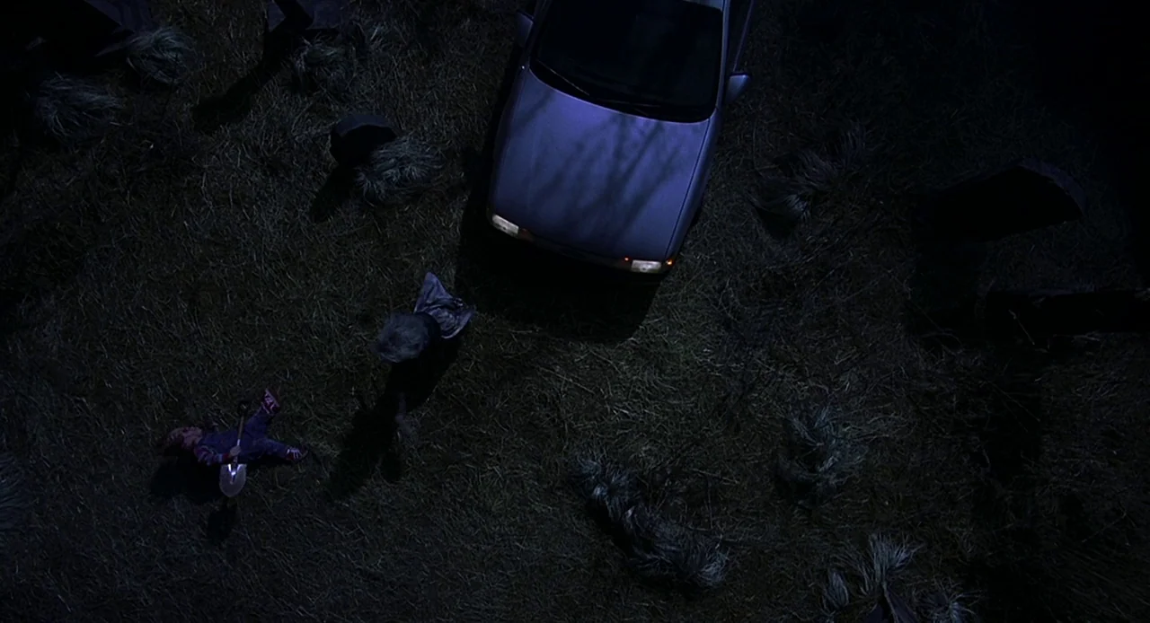 Bride of Chucky (1998) movie still: wide — A dark, grassy cemetery at night with scattered headstones and unkempt vegetation. A parked car…