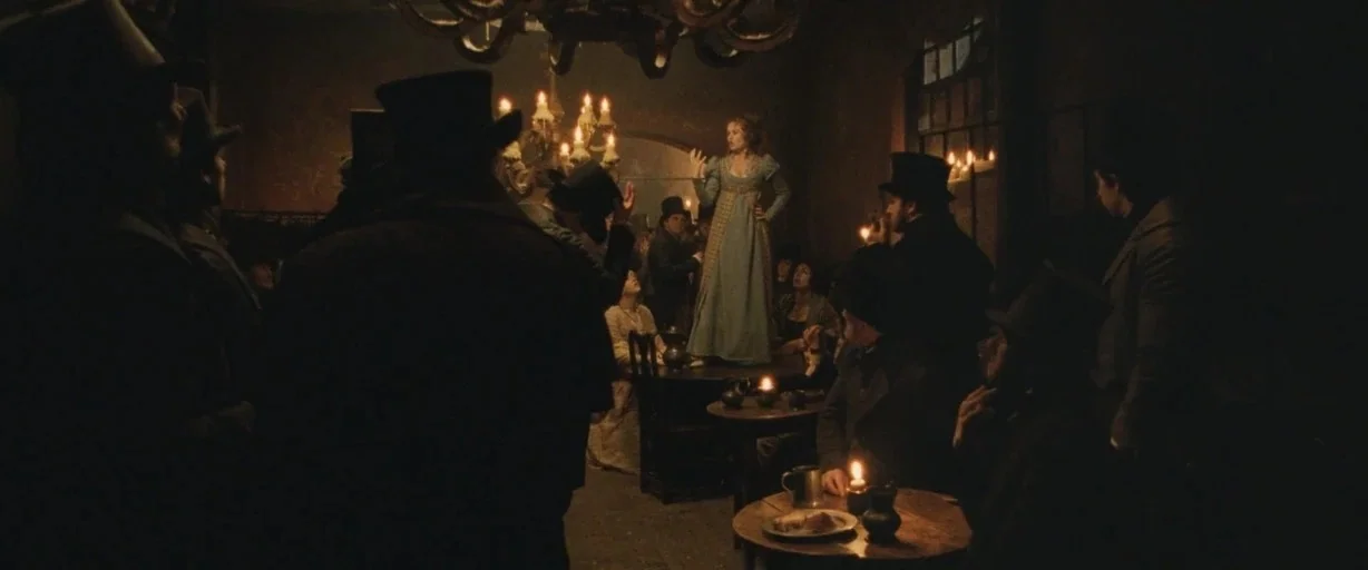 Burke & Hare (2010) movie still: wide — A dimly lit 19th-century tavern filled with patrons wearing top hats and period clothing. A woman in a blue…