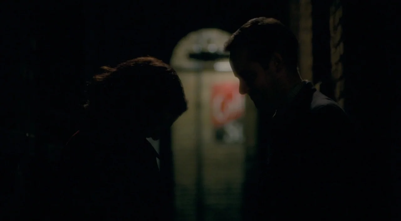 The Deep Blue Sea (2011) movie still: medium — Two individuals stand in a dimly lit, narrow outdoor passage at night. The pair is positioned in…