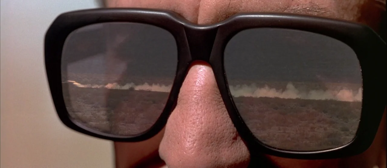 Casino (1995) movie still: closeup — A close-up view of a person's nose and eyes hidden behind dark sunglasses. The desert landscape with a dust…