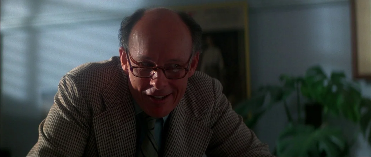 The Monster Squad (1987) movie still: medium — An interior space with a houseplant in the background and soft light filtering through. A balding…
