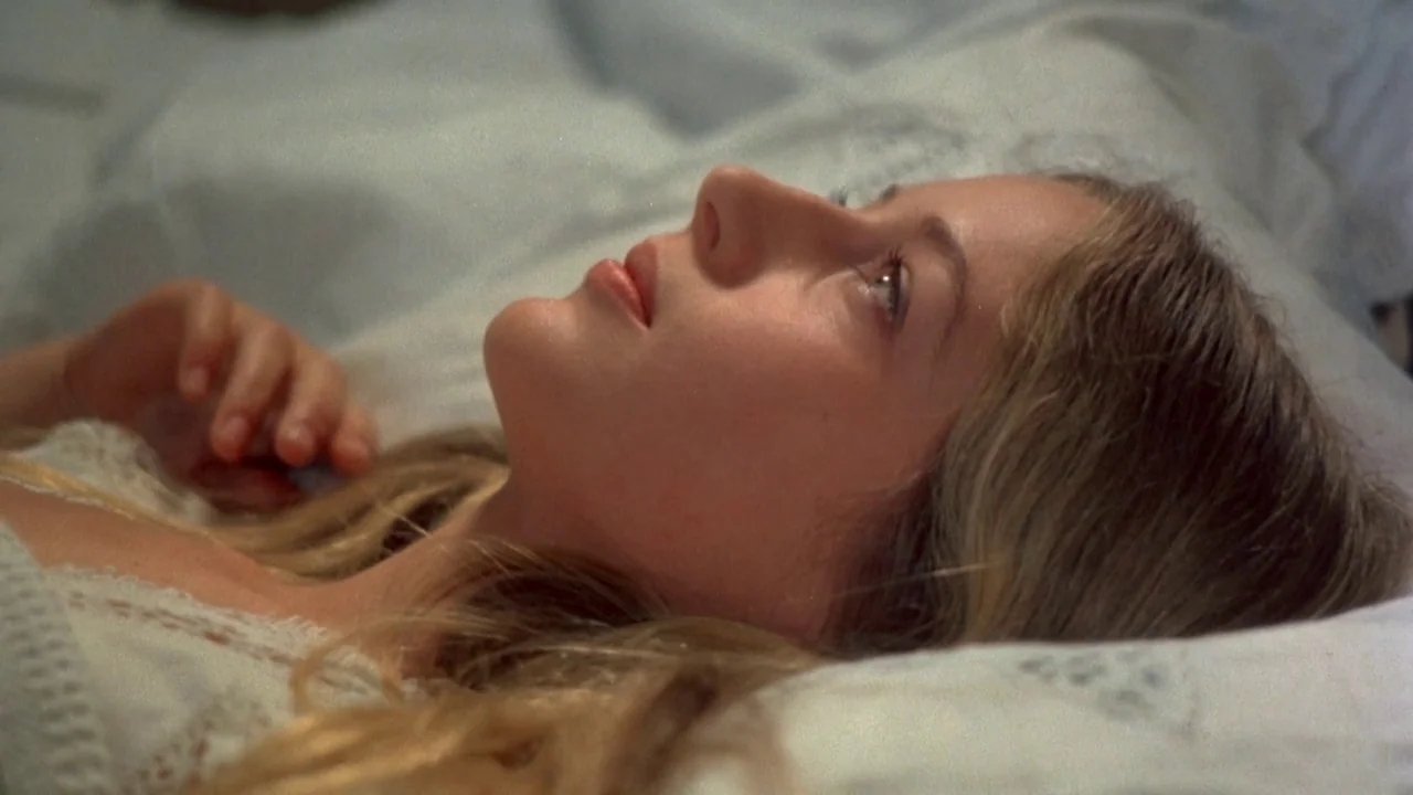 Picnic at Hanging Rock (1975) movie still: closeup — A woman lies on a bed with white bedding and lace pillows. The subject is resting her head on…