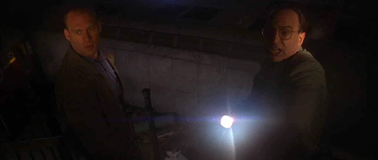 Die Hard with a Vengeance (1995) movie still: medium — An outdoor concrete stairwell at night is submerged in total darkness. Two men stand in the…