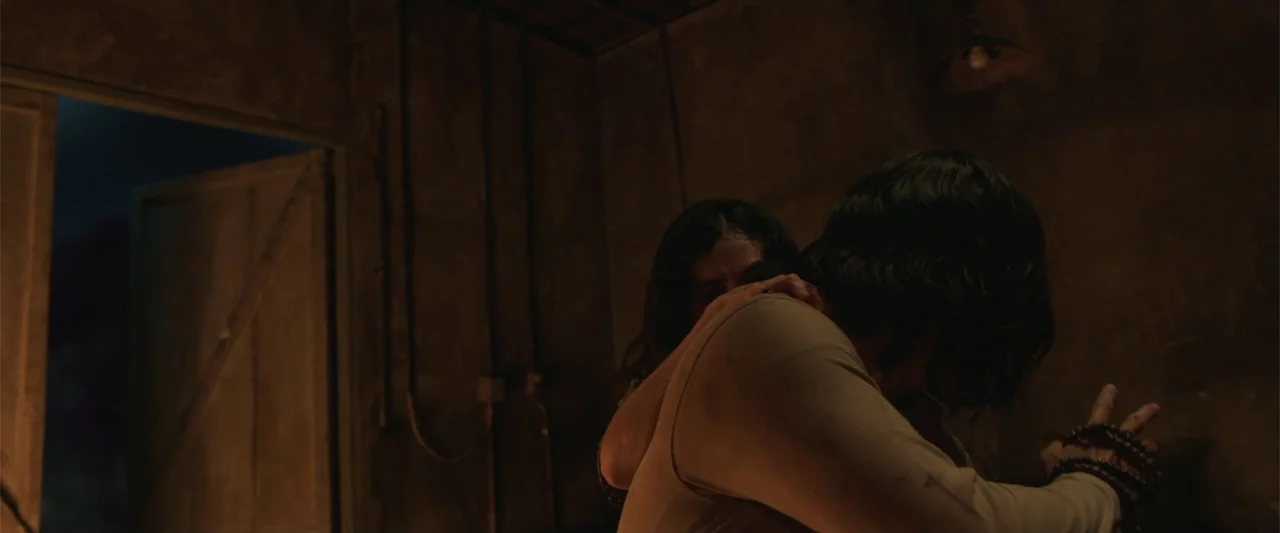 The Unholy (2022) movie still: medium — A dimly lit room with plain walls and a single open doorway leading outside. A man in a light shirt stands…