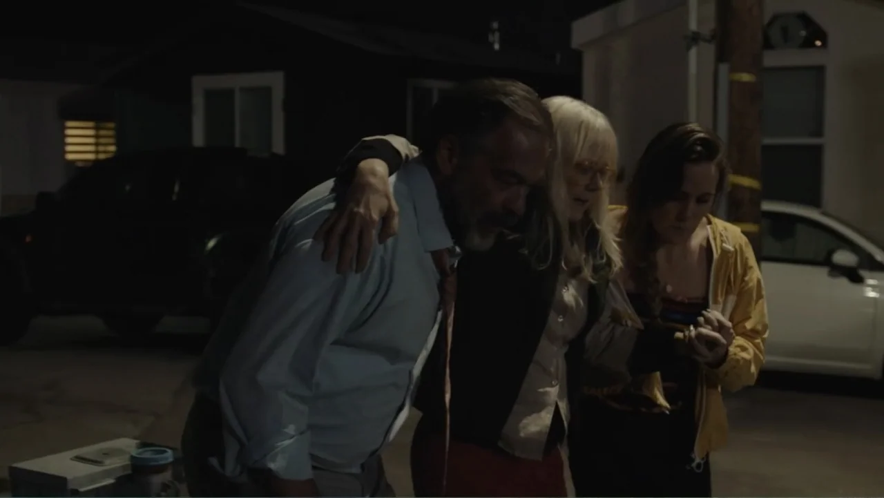 The Cleaner (2021) movie still: medium — A night exterior scene shows a parking lot with a vehicle in the background. A man and a woman help an…