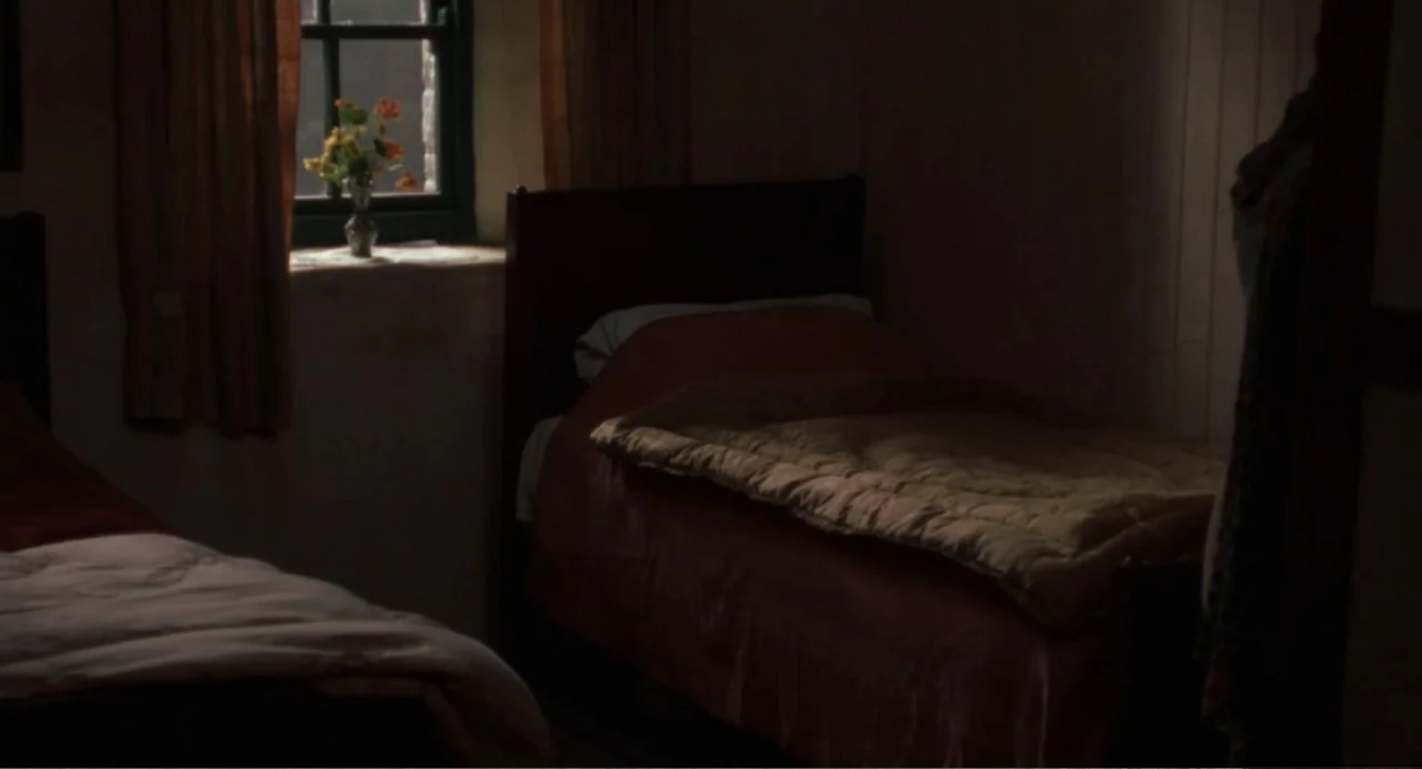Dancing at Lughnasa (1998) movie still: wide — A dark, sparsely furnished bedroom contains two wooden beds with quilts. Daylight enters through a…