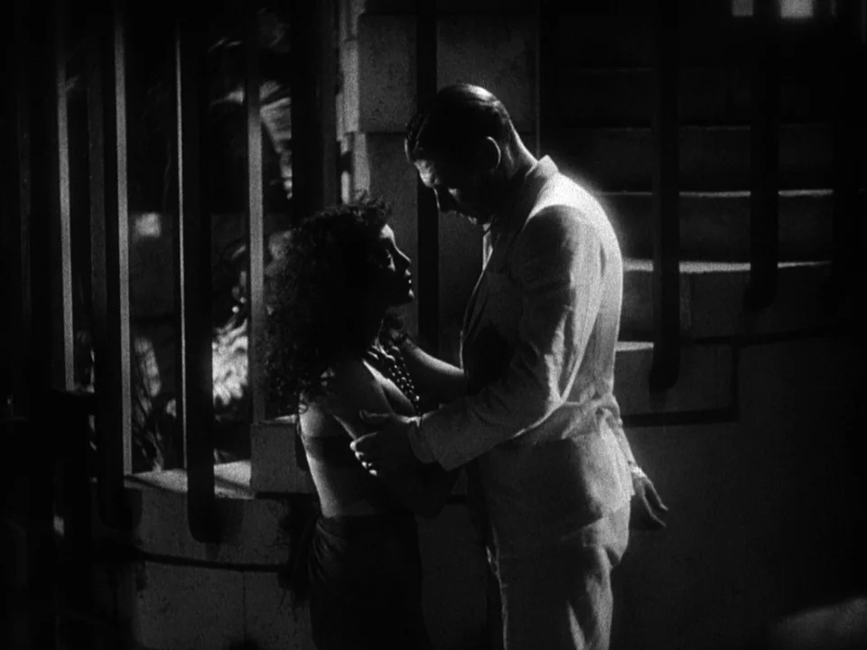 Island of Lost Souls (1932) movie still: medium — A dark staircase landing with heavy vertical metal bars in the background. A man in a suit stands…