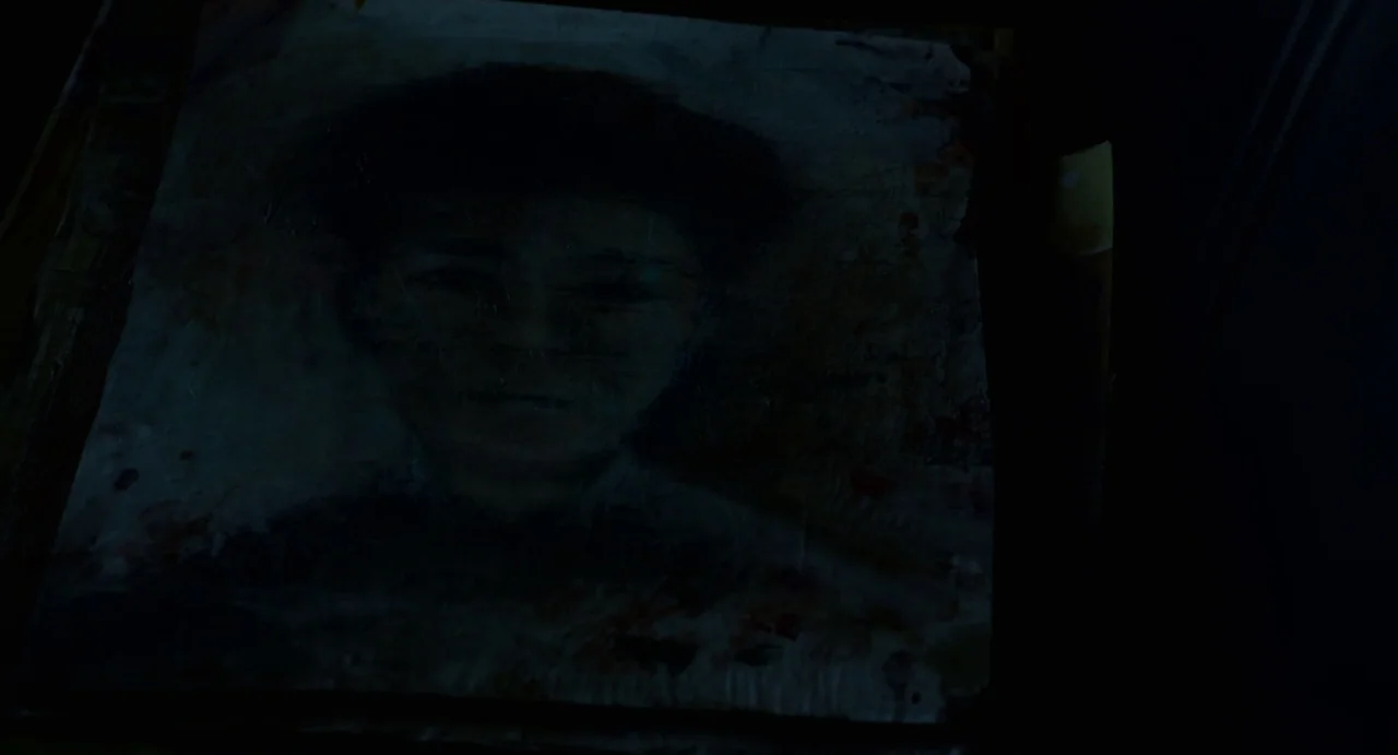 Velvet Buzzsaw (2019) movie still: closeup — A dimly lit, weathered painting of a person rests within a dark environment. The painted subject stares…