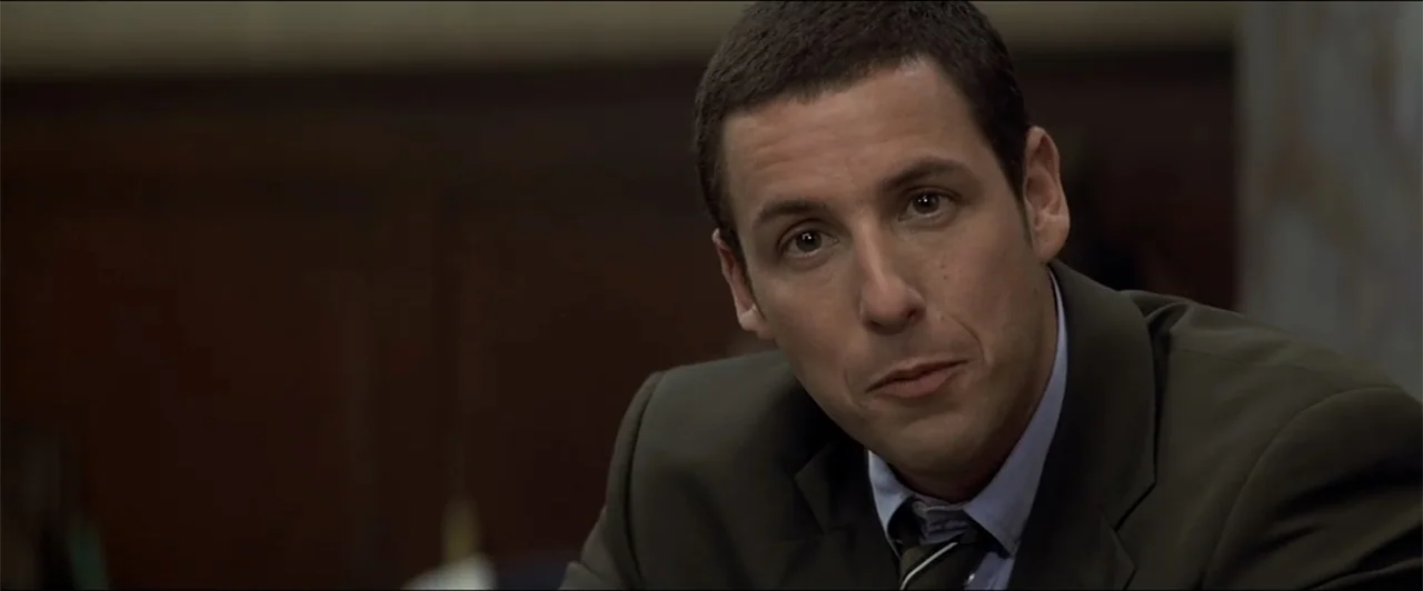 Anger Management (2003) movie still: closeup — An interior office space features dark wood paneling on the wall behind the subject. A man in a dark…
