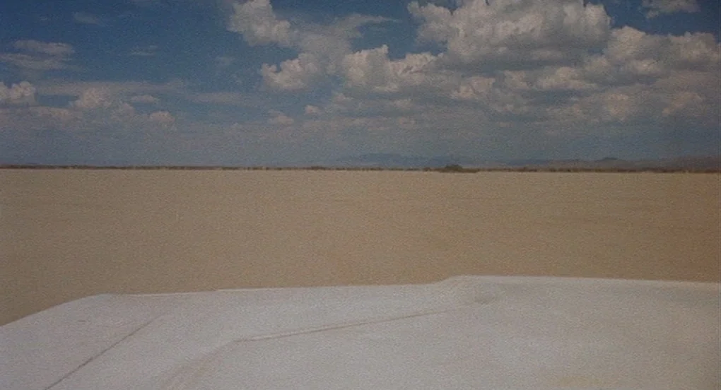 Vanishing Point (1971) movie still: establishing — A vast, flat desert plain stretches toward a distant, low-lying horizon under daylight. A white…