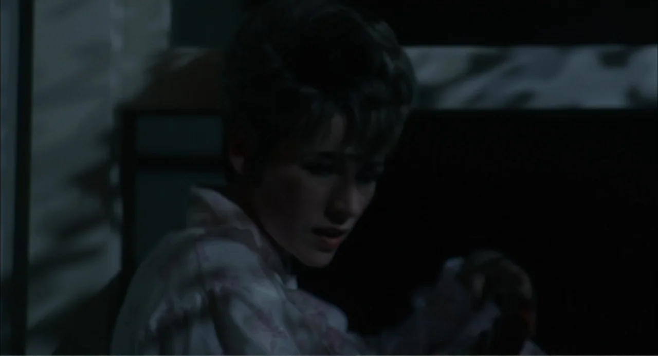 Cottonpickin' Chickenpickers (1967) movie still: closeup — A dimly lit room with patterned walls and a dark, shadowed background area. A young woman…