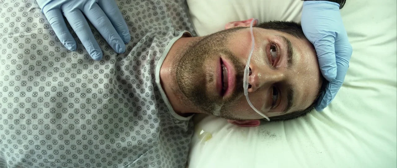 Universal Soldier: Day of Reckoning (2012) movie still: closeup — A man in a hospital gown lies prone on a white pillow. Medical personnel in blue…
