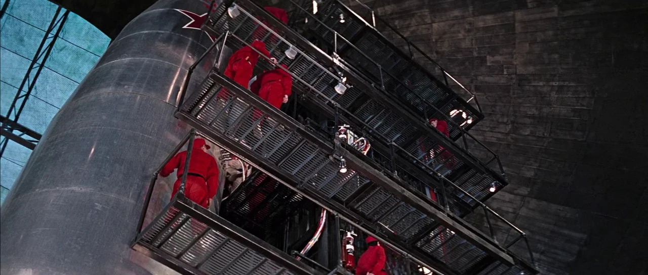 You Only Live Twice (1967) movie still: wide — A dark industrial interior features a massive silver rocket structure with tiered metal walkways.…