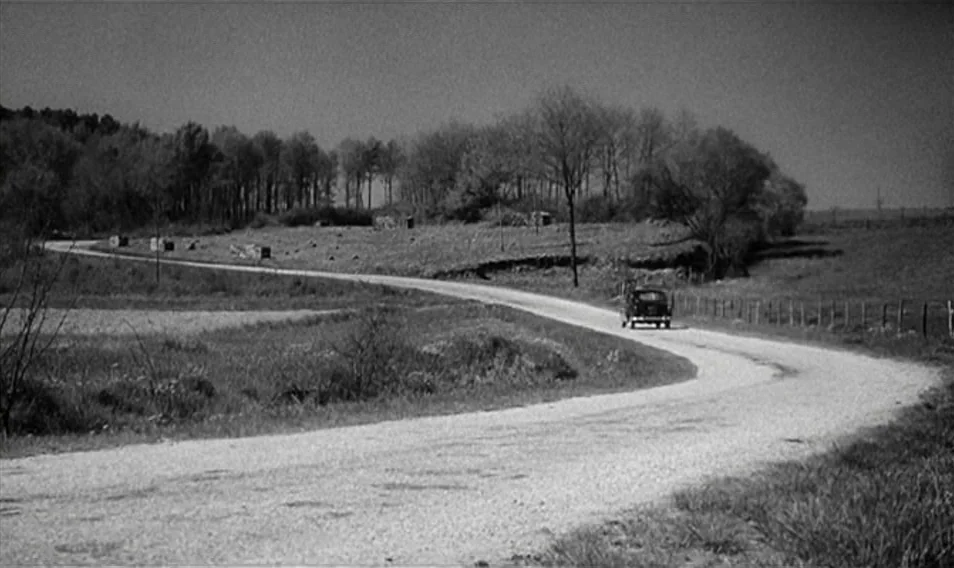 Thérèse Desqueyroux (1962) movie still: wide — A black and white view of a winding dirt road through rural fields. A lone vintage car travels along…
