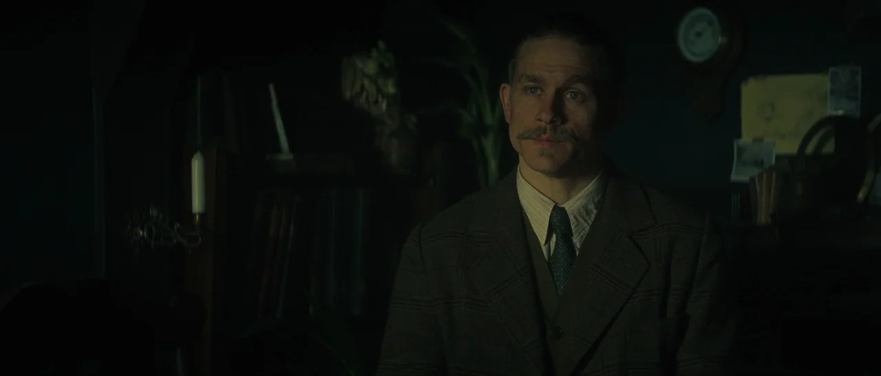 The Lost City of Z (2016) movie still: medium — A dark study contains a bookshelf, an analog wall clock, and various personal items. The man stands…