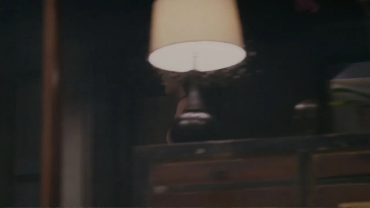When a Stranger Calls (2006) movie still: medium — A dimly lit room contains a wooden cabinet topped with a lit table lamp. A woman is visible…
