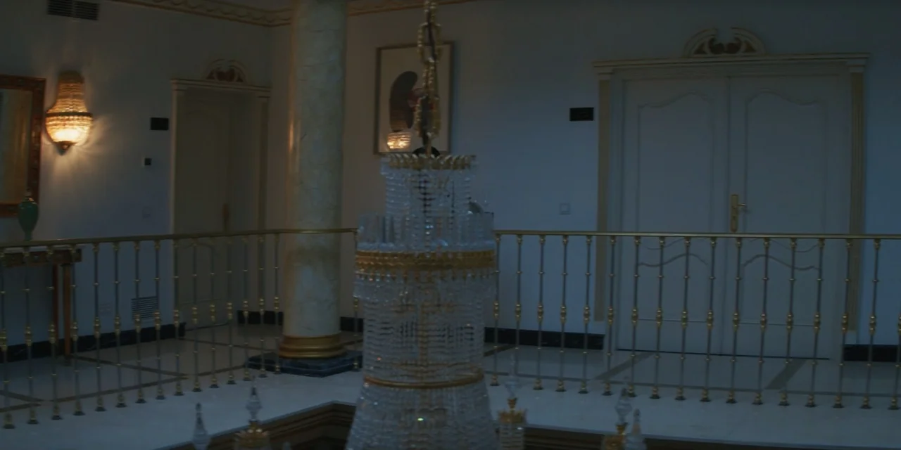 My Fault (2023) movie still: medium — A hotel corridor landing features a large crystal chandelier in the foreground out of focus. A marble column…
