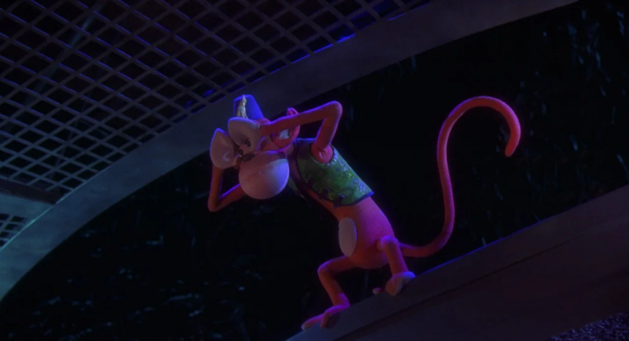 Monkeybone (2001) movie still: medium — An orange monkey character stands on a dark, overhead wooden rafter in an attic. The character has a hand…