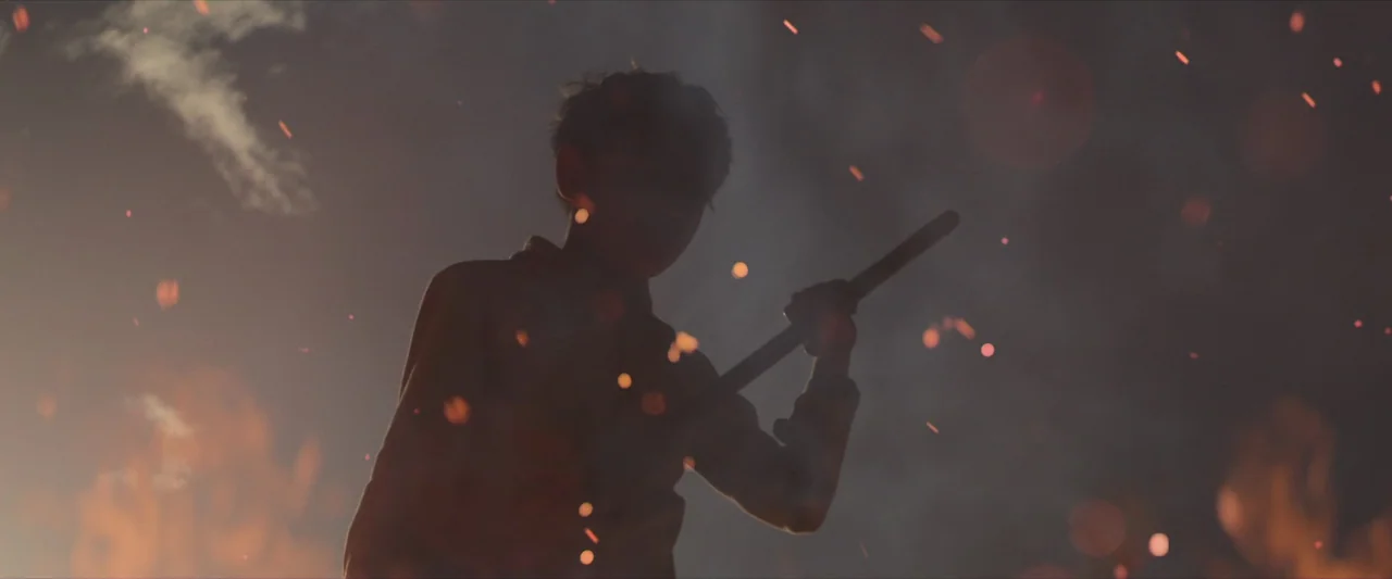 The New Boy (2023) movie still: medium — A person stands amidst a dark environment filled with floating embers and smoke. The figure is silhouetted…
