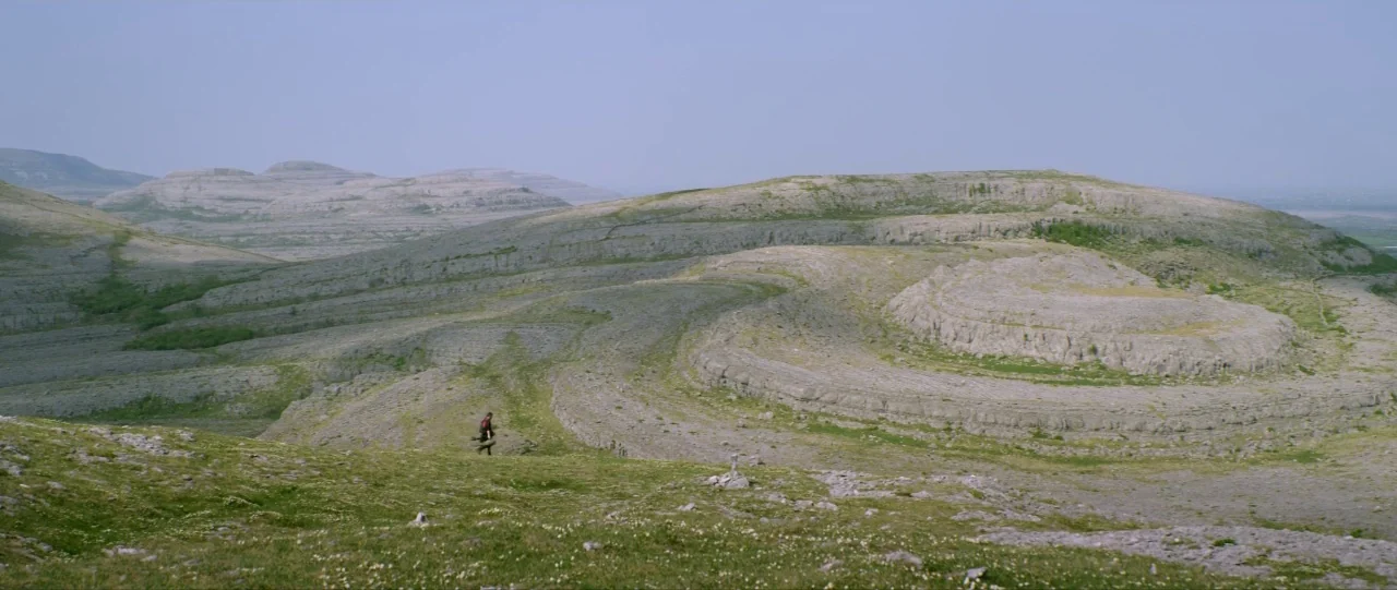 Silence (2012) movie still: wide — A vast, expansive landscape characterized by terraced limestone hills and patches of low grass. A solitary person…
