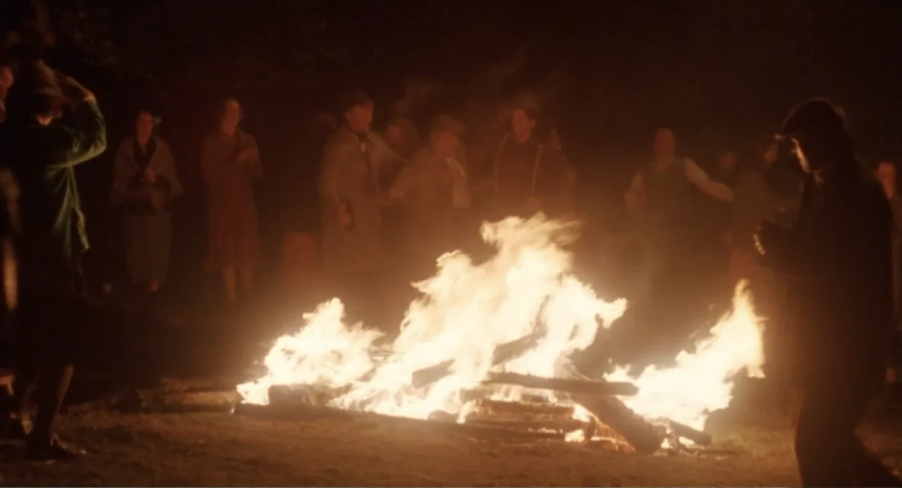 Dancing at Lughnasa (1998) movie still: wide — A group of people stands in a circular formation around a large roaring bonfire. The figures are…