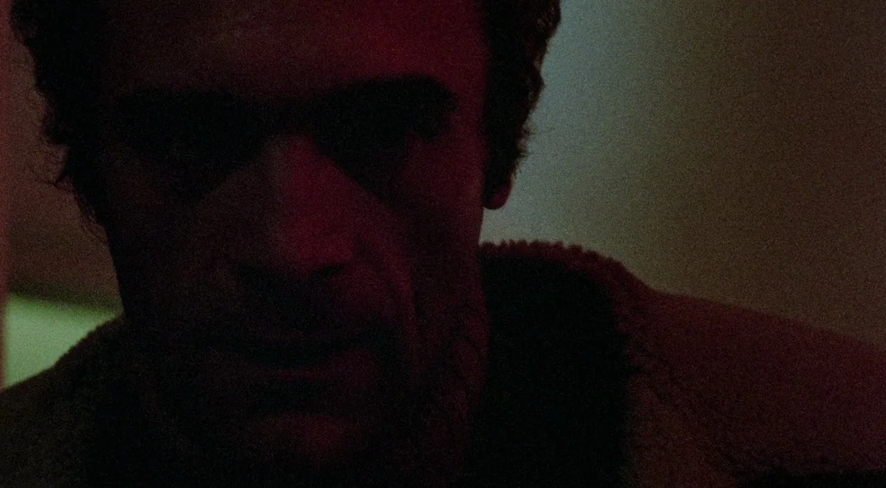 The Iguana with the Tongue of Fire (1971) movie still: closeup — A dimly lit interior space with a man's face illuminated by red light. The man…