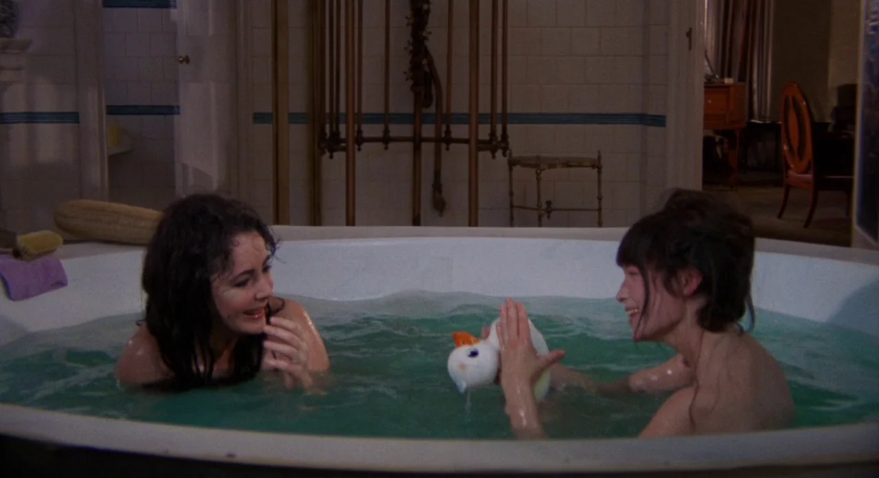 Secret Ceremony (1968) movie still: medium — A spacious bathroom features tiled walls and a large, central, oval-shaped pedestal tub. Two women sit…