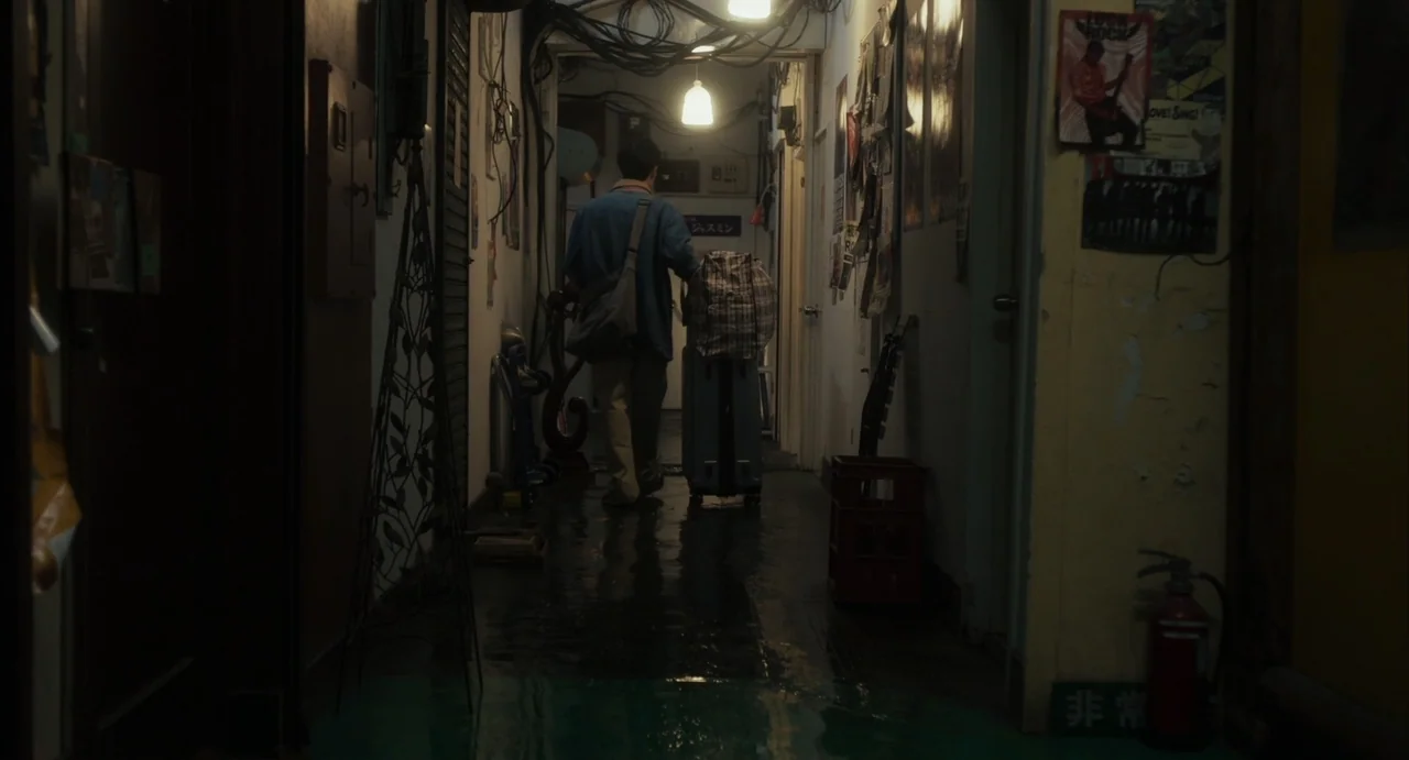 Stigmatized Properties: Possession (2025) movie still: fullbody — A narrow, cluttered apartment corridor with exposed wiring and walls covered in…