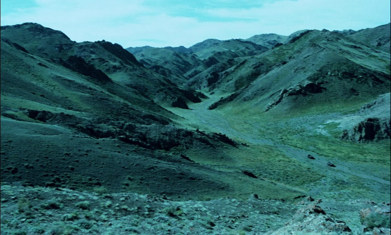 On The Silver Globe (1988) movie still: establishing — A deep mountain valley stretches toward the horizon between steep, rocky, green slopes. Two…