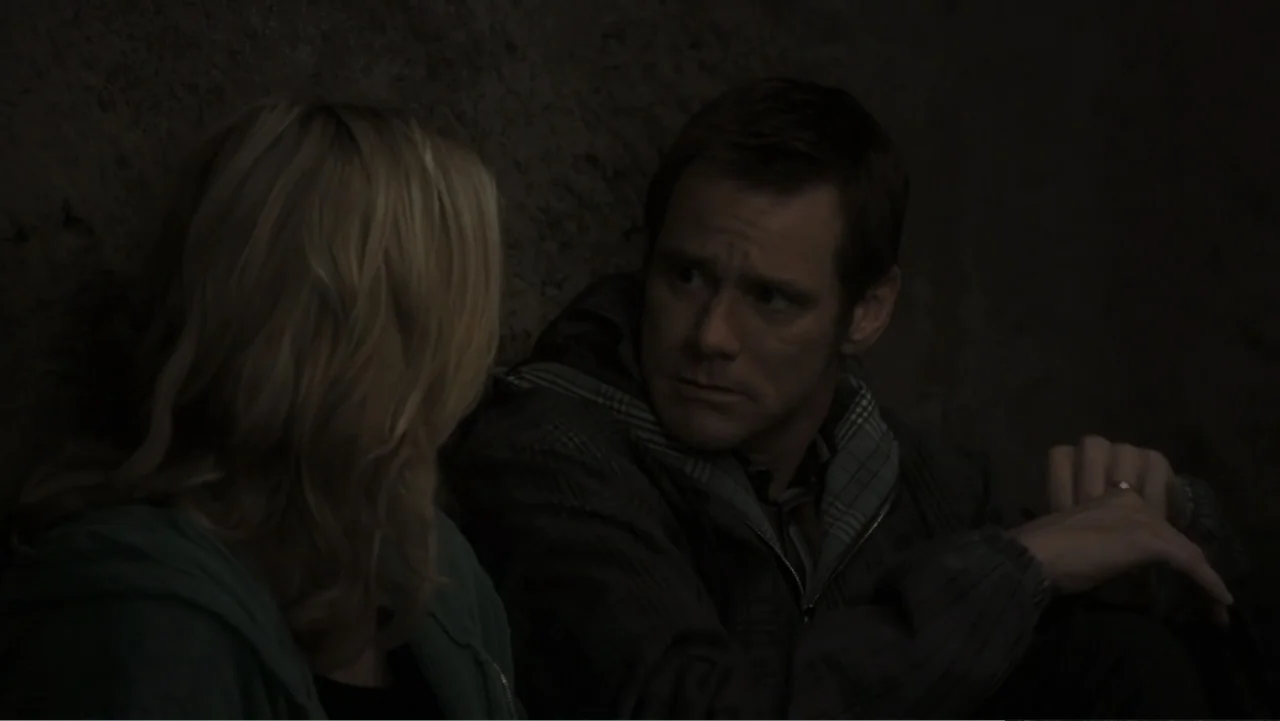 Fun with Dick and Jane (2005) movie still: medium — A dimly lit interior room with stone-like textured walls in darkness. A man and a woman sit in…