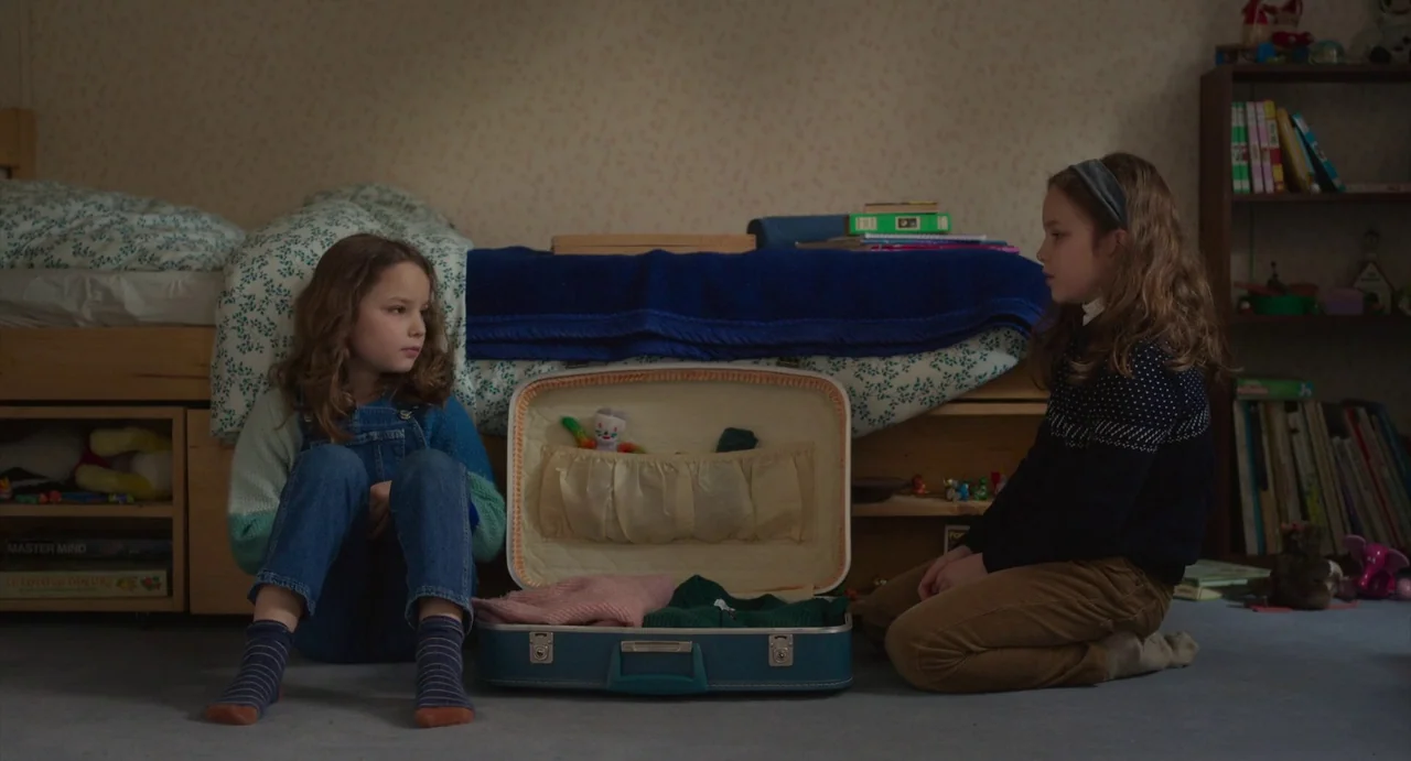 Petite Maman (2021) movie still: medium — A cluttered child's bedroom features a bed frame with shelves underneath filled with toys. Two young girls…