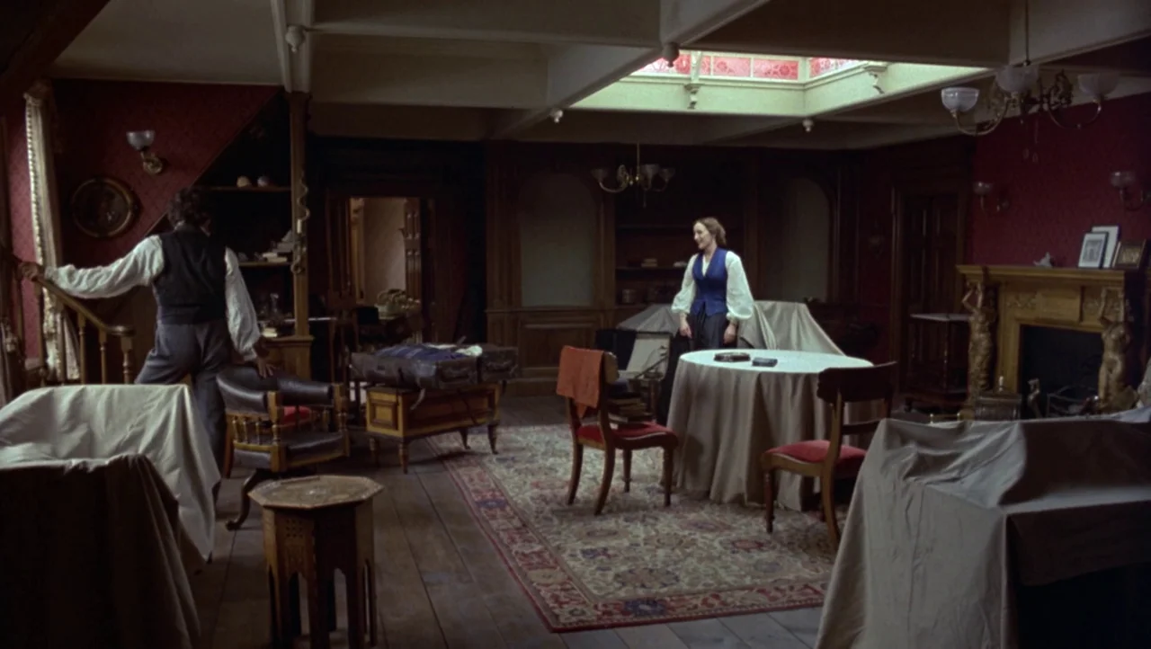 Mountains of the Moon (1990) movie still: wide — A spacious Victorian parlor features dark red wallpaper, wooden floors, and furniture draped in…