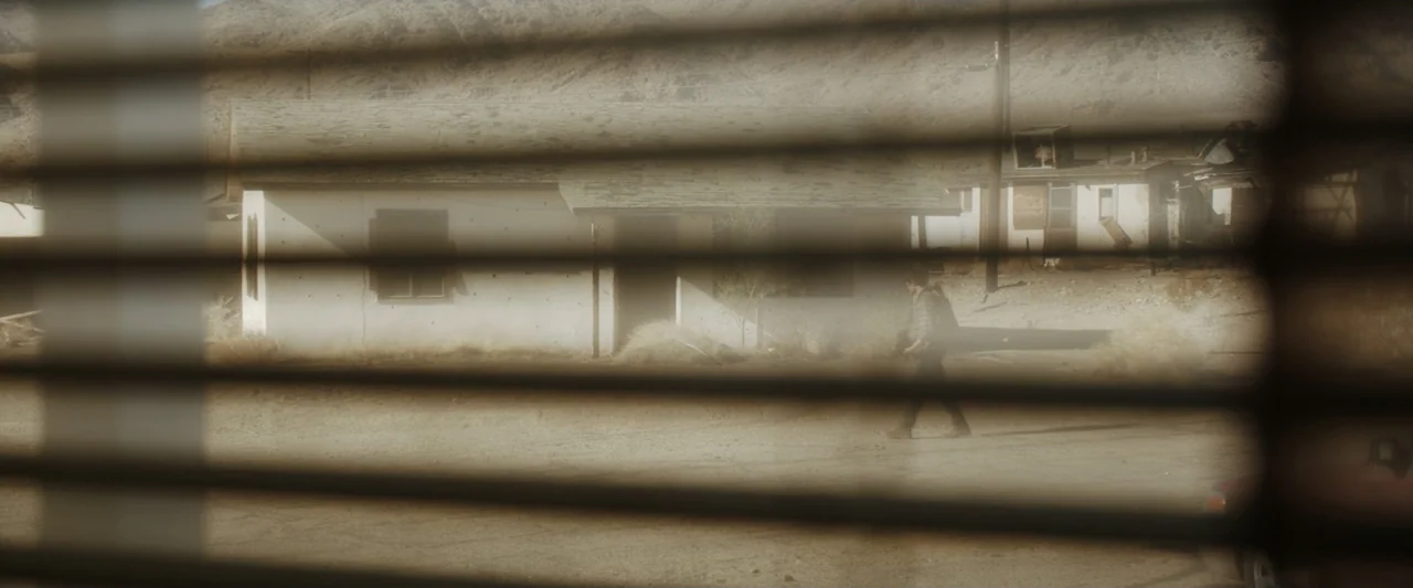 Encounter (2018) movie still: wide — A remote desert settlement features a single-story white building under bright sunlight. A lone man walks…