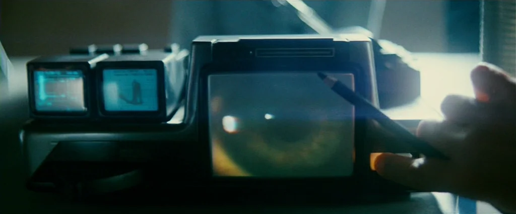 Blade Runner (1982) movie still: closeup — A complex electronic device with multiple small monitors sits on a dark surface. A hand enters from the…