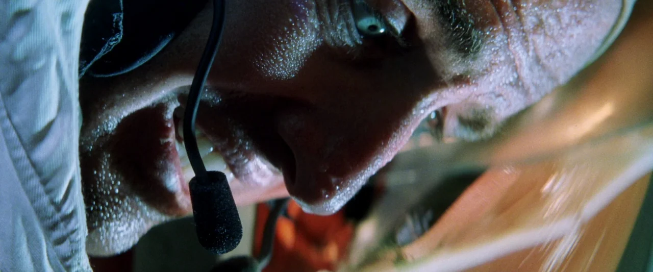 Armageddon (1998) movie still: closeup — A close-up view of a man inside a cramped, dark aviation environment. He is yelling while wearing a headset…