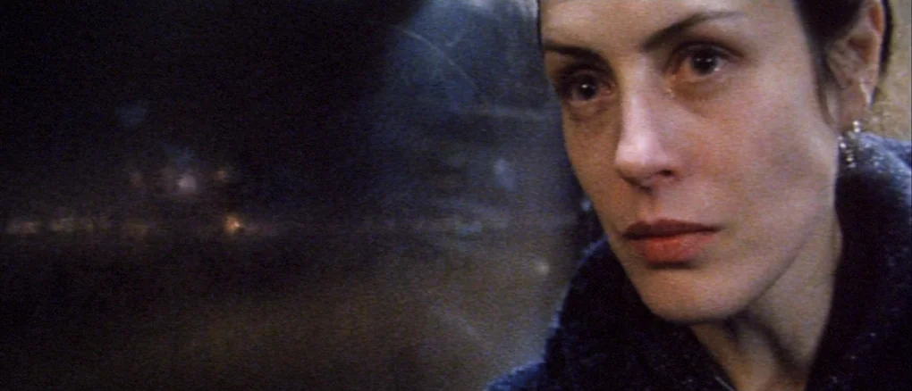 Wonderland (1999) movie still: closeup — A dark, out-of-focus background shows faint city lights moving past a window pane. A woman looks out the…