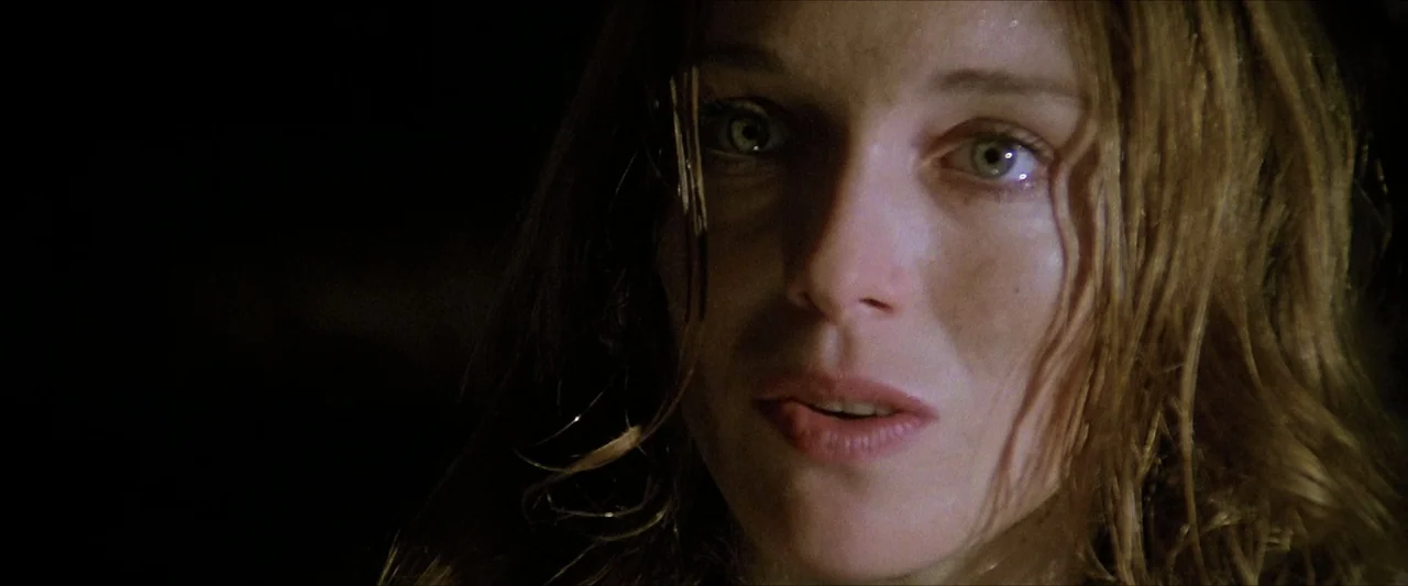 The Beyond (1981) movie still: closeup — A woman's face is illuminated from the side in a dark, undiscernible setting. She gazes forward with a…