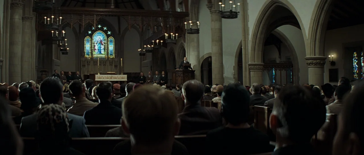 Changeling (2008) movie still: wide — A stone cathedral interior filled with a congregation of people in 1940s attire. A man stands at a wooden…