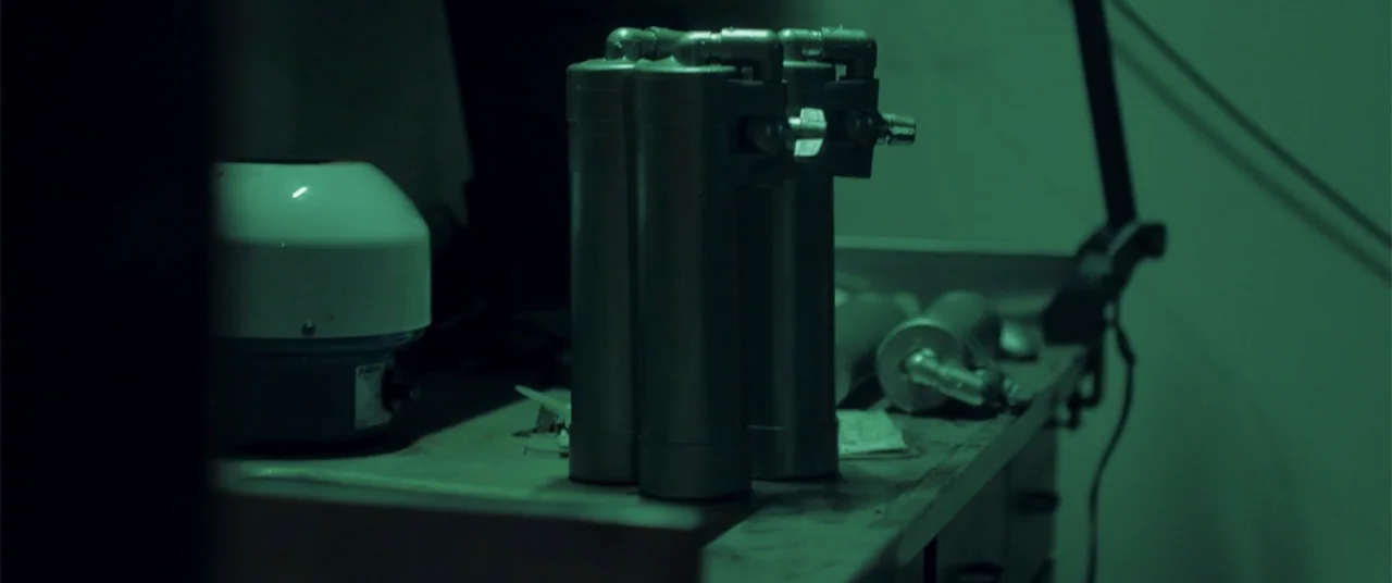 Phobias (2021) movie still: medium — A laboratory workbench holds several metal canisters and a centrifuge device. The scene is illuminated in a…