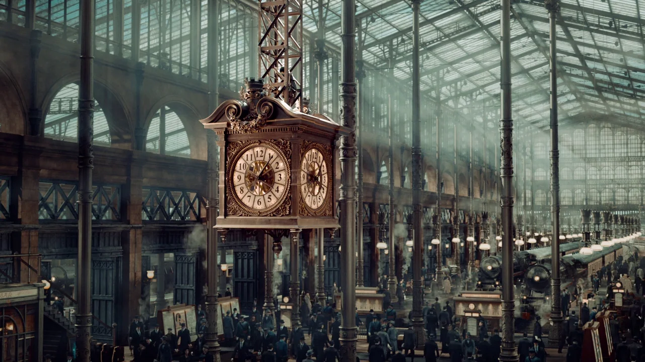 Hugo (2011) movie still: establishing — A vast, high-ceilinged train station features extensive ironwork, large glass panes, and steam engines. An…