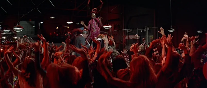 Sweet Charity (1969) movie still: wide — A dark warehouse interior is filled with a large crowd dancing in red light. A man in a pink patterned…