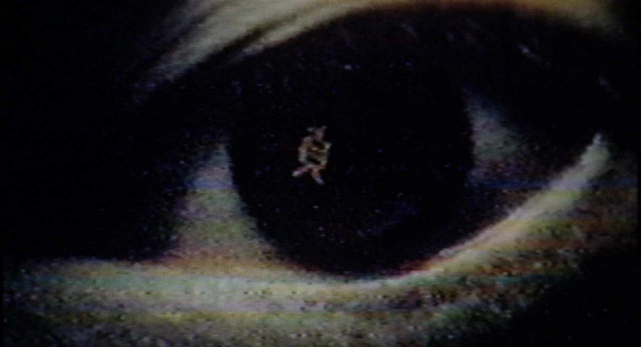 Ringu (1998) movie still: closeup — An extreme close-up of a human eye features a small, pale geometric shape suspended within the dark pupil. The…