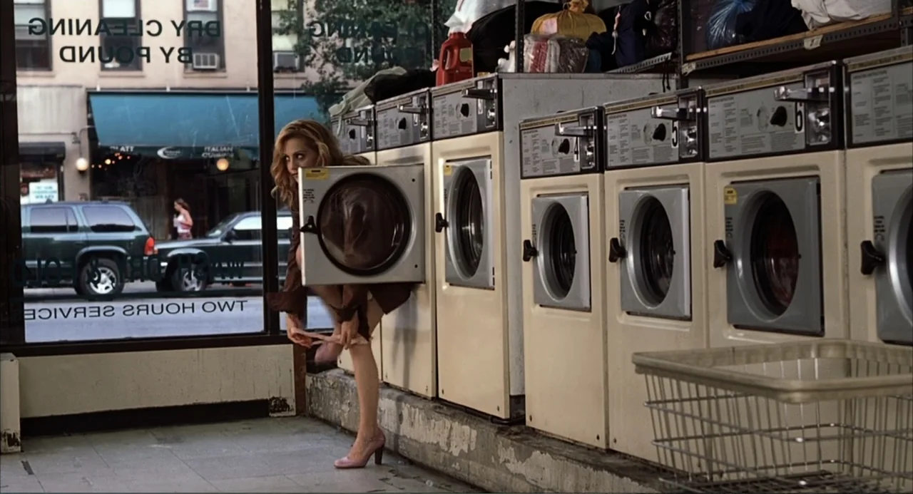 Uptown Girls (2003) movie still: medium — A urban laundromat features a row of white machines and a large storefront window. A young blonde woman…