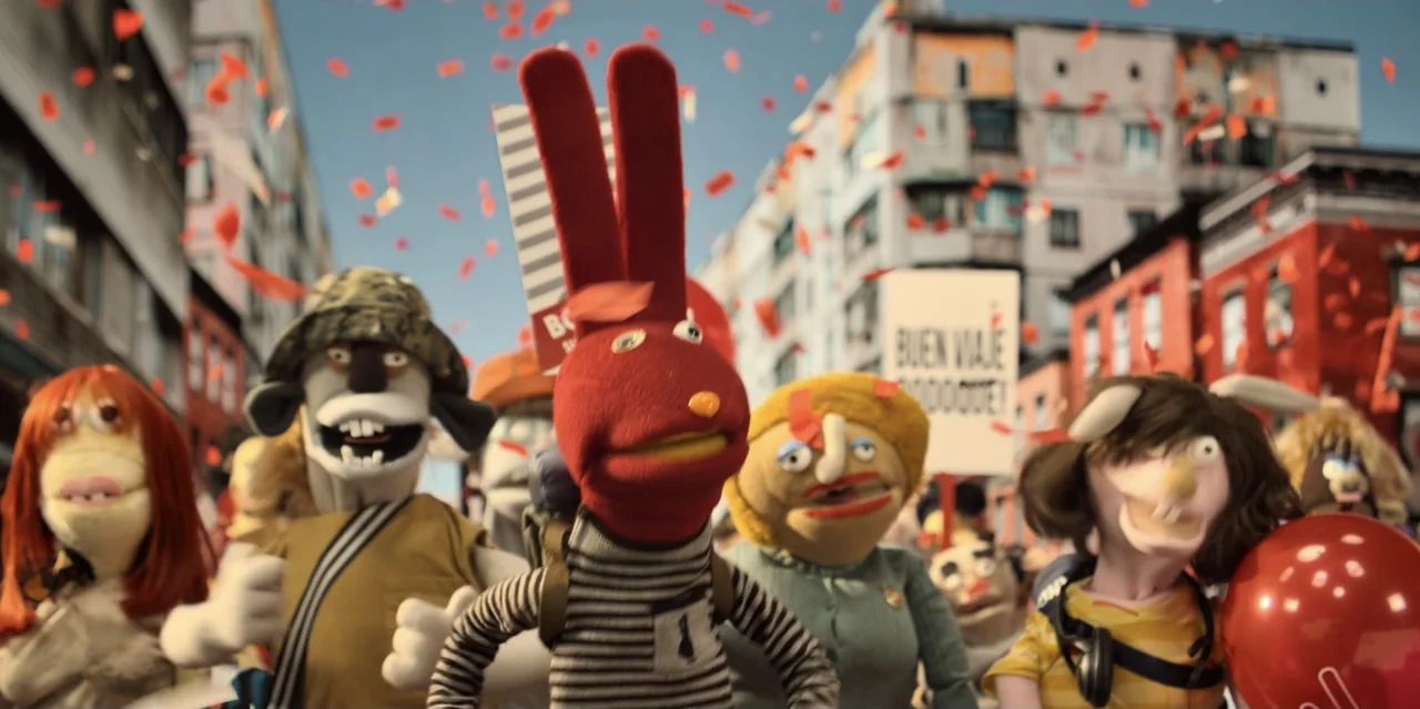 31 Minutes: One Hot Christmas (2025) movie still: medium — A diverse group of stylized puppets parades down a residential city street. They walk…