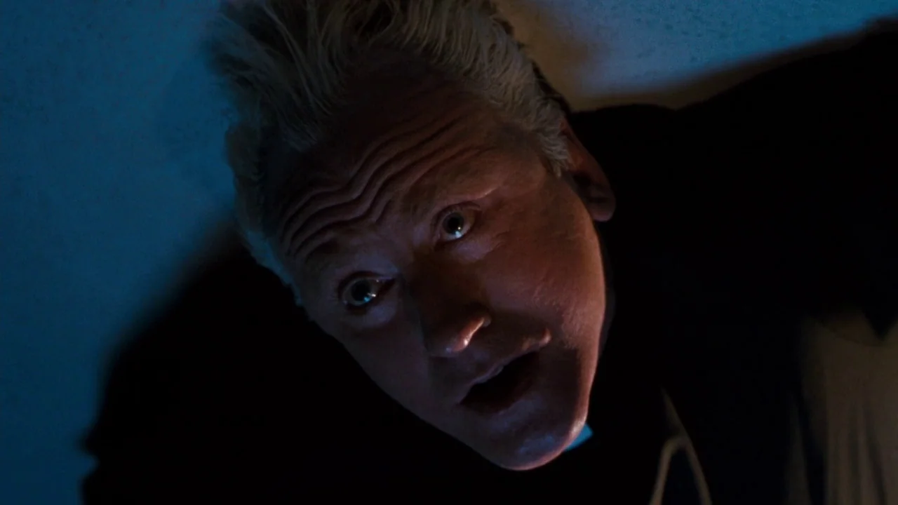 The Exorcist 3 (1990) movie still: closeup — A close-up view of a man's face illuminated from below in darkness. He looks upward toward the viewer…