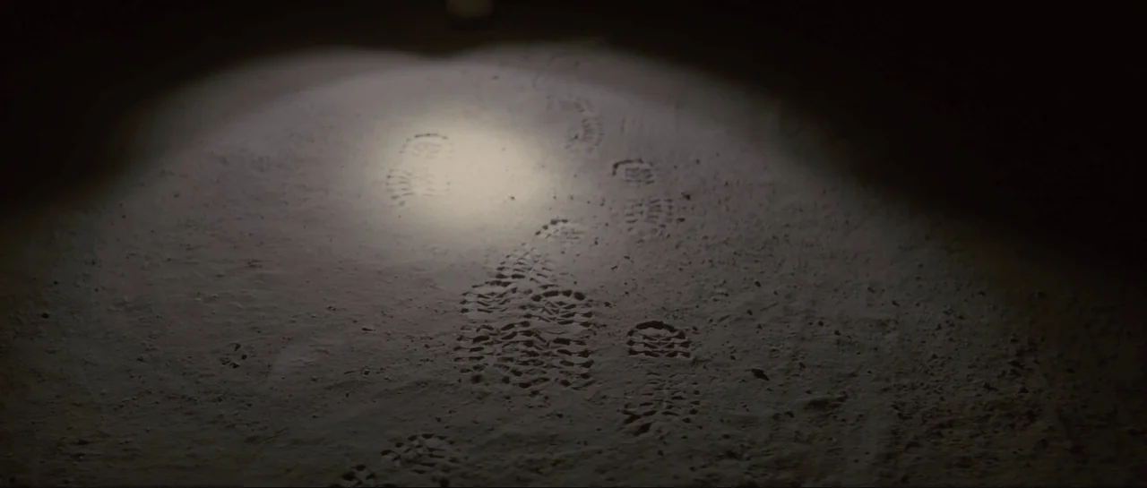 The Last Days On Mars (2013) movie still: closeup — A dark, uneven earthen surface shows several distinct boot prints in the fine dust. A tight beam…