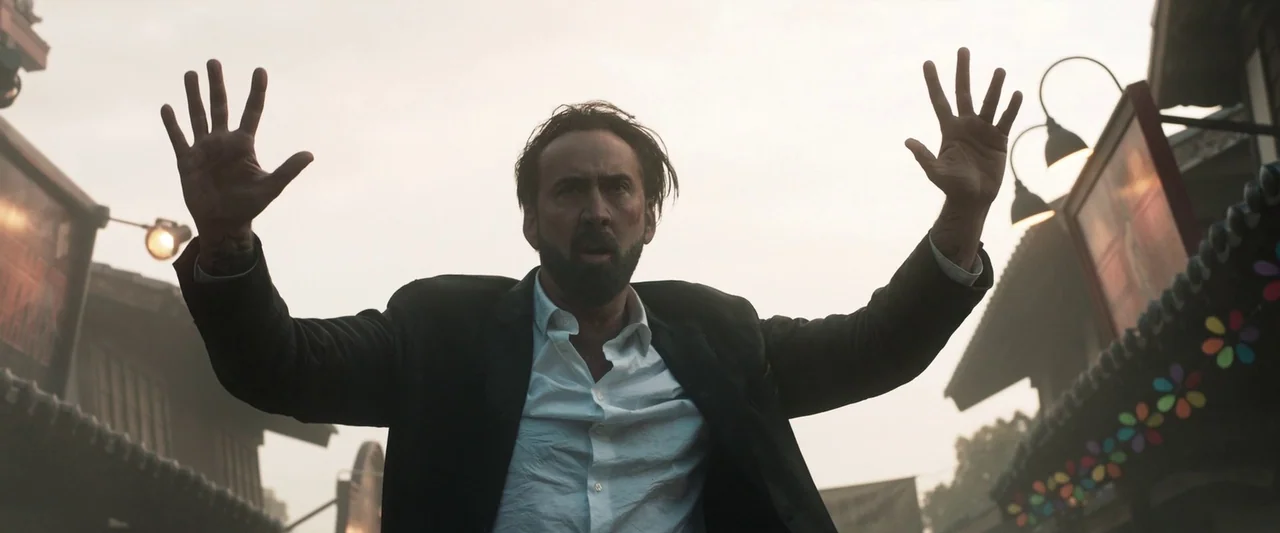 Prisoners of the Ghostland (2021) movie still: medium — A fairground at dusk features blurred stalls with hanging string lights in the background. A…