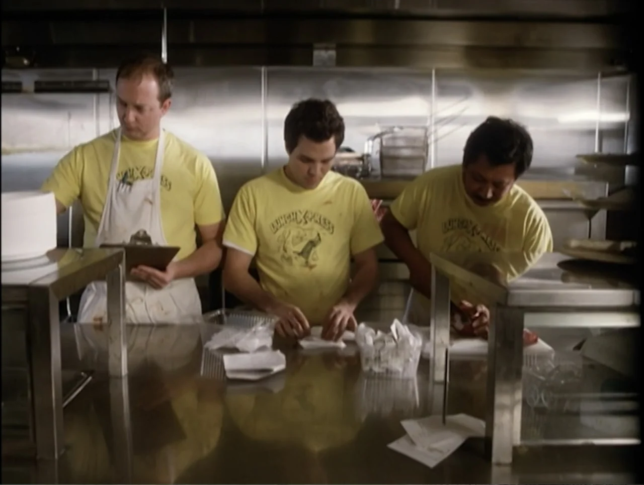 Apartment 12 (2001) movie still: medium — A professional food service station features stainless steel surfaces and metallic backsplashes. Three men…